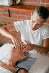 Senior woman receiving a facial massage from a beautician in a white t shirt