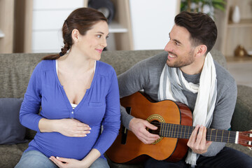 Fototapeta premium man practicing guitar with pregnant woman