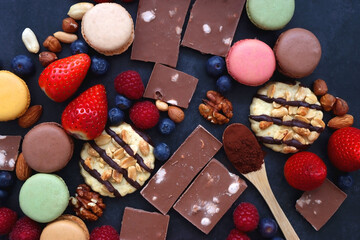 Macarons, chocolate, cookies, berries and various nuts on dark blue background. Top view.