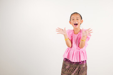 Portrait Thailand kid girl smiling traditional Thai dress costume raises fists in celebration of her success, studio isolated white background, kindergarten child saying yes with excitement winning