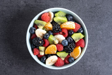 Fruit salad in a blue bowl on black slate background. Top view