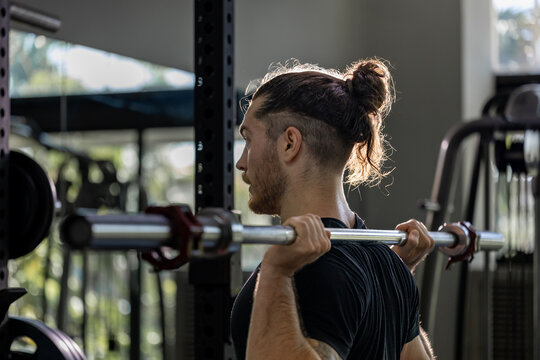 Caucasian muscular body builder sport man is practice weight training on squat barbell for core muscle inside gym with dark background for exercising and workout usage