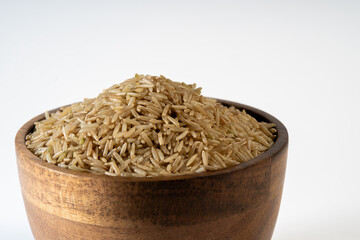 Uncooked brown Basmati rice grains in wooden bowl, healthful and natural, against white background. Copy space.