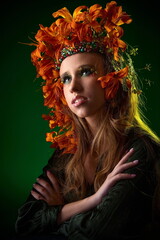 A young girl with beautiful hands, exquisite makeup and good skin, decorated with red lilies in her hair, poses in the studio against a dark green background.