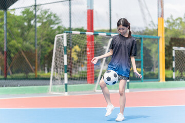 Asian child girl playing football in the urban outdoor futsal court