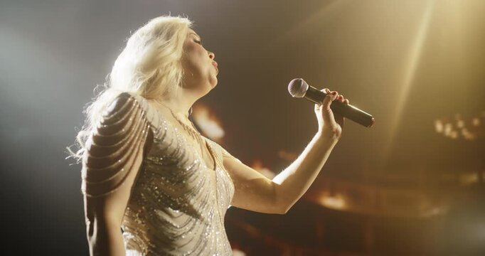 Pop Singer Performing on a Live Concert Stage. Portrait of an Adult Female Wearing a Striking Dress Covered with Glitter, Singing a a Deep Romantic Song into the Microphone