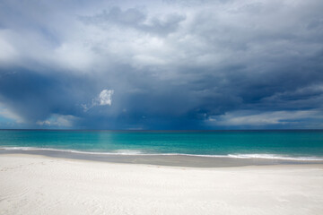 Dark storm clouds approaching a white, sandy beach over turquoise waters in the Bay of Fires, Tasmania.