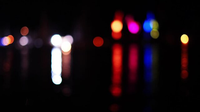 Slow motion of blurred lights of ships, boats and cranes reflecting on water surface at night. Colourful minimalistic bokeh background. Abstract evening city seaport scenery from Pula, Croatia.