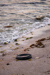 Old car tires on the beach,Water and sea coast pollution car tires on sand beach,An image of an old car tire ingrown into the sand.Old car tires with seaweed stuck on.