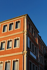 Obraz premium Orange Building Corner with Evening Sunlight. Corner of an orange building illuminated by evening sunlight against a clear blue sky. Highlights architectural elements and color contrast.
