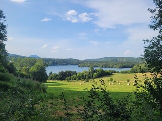 Obraz premium Wide shot of green meadow with bales of hay and a lake in the background 