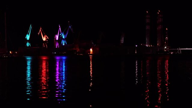 Lighting Giants - colourful illuminated cranes in Pula, Croatia. Lights of ships, boats and cranes reflecting on water surface at night. Industry and transport harbour, evening city seaport scenery.