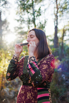 young girl plays the harmonica in the forest. girl enjoys playing a musical instrument in the forest.