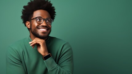 Obraz premium A cheerful man with curly hair and glasses smiles warmly, dressed in a green sweater and posing against a matching green background. Perfect for themes of joy, positivity, and relaxation.