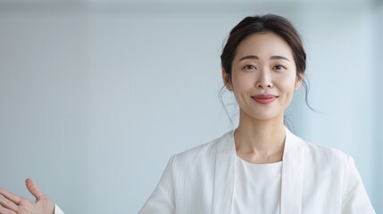 A professional Asian woman standing with a smile, arms open, looking at the camera, a soft-focus minimalist office space.