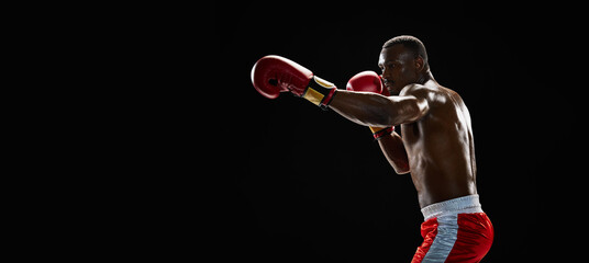 Muscular focused African-American man with shirtless body practicing boxing stances, training...