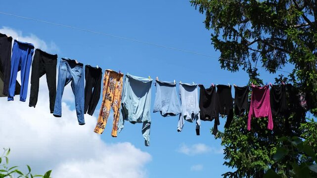 Colourful wet clothes hanging on a clothesline and moving by the wind. Drying washed laundry outdoors on the street between an old apartment building and a huge tree. Simple city life in Croatia.