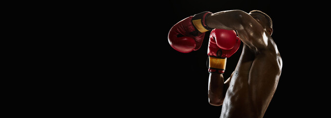 Muscular African-American man, boxer showing his perfect left hook, training isolated on black...