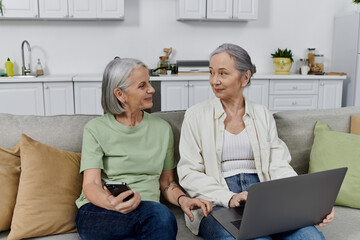 Two mature lesbian women rest on a couch after cleaning their modern apartment together.