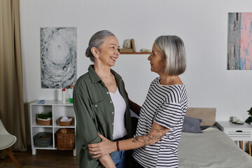 Fototapeta premium Two mature women, a lesbian couple, embrace each other in a modern apartment, their smiles radiating happiness and love.