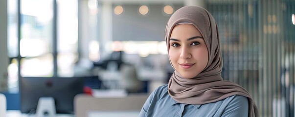 Fototapeta premium Portrait of a woman in a hijab, standing confidently in a modern, welllit office
