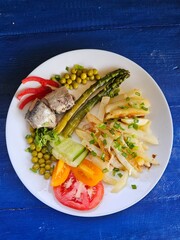 Dish with fried potatoes, asparagus, vegetables and fish on a blue background