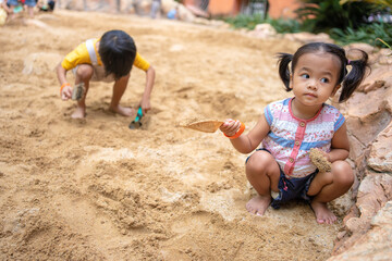 Asian kindergarten boy and girl enjoy playing in sandbox having fun on playground in sandpit.