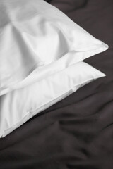 White satin (lyocell, silk, polyester) pillowcases on the bed covered with dark grey sheet. Home textile.