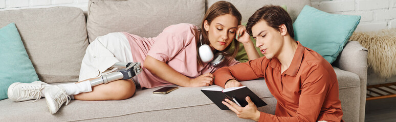 A woman with a prosthetic leg and her boyfriend relax on a couch, sharing a book together.