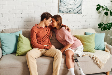 A woman with a prosthetic leg and her boyfriend share a tender moment on a sofa.