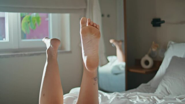 Closeup playful woman legs in bedroom sunlight. Happy girl dangling feet at home