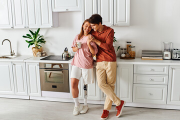 A woman with a prosthetic leg enjoys a coffee with her boyfriend in their kitchen.