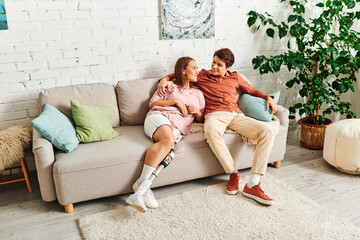 Woman with prosthetic leg smiles at boyfriend on couch.