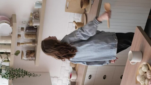 young woman in a denim jacket enjoys an impromptu karaoke session in her kitchen, using a wooden spoon as a microphone. This image showcases the fun and spontaneity of enjoying music at home.