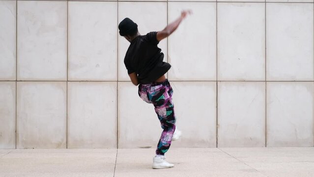 Street performer impressively breakdancing, handstand in urban setting against white wall
