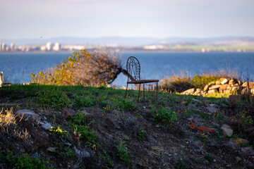 A lone chair on a hill at sea. Lonely chair concept. City and hills in the background. A person can sit and watch the sea horizon.