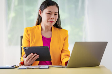 An Asian businesswoman is diligently working at an accountant's desk, surrounded by financial documents and a laptop, meticulously analyzing data to ensure accurate and efficient financial management.