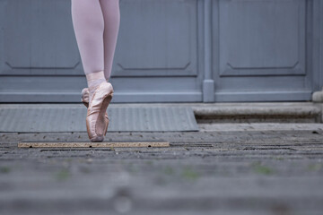 Closeup of a dancer legs balancing on the pointe shoes. Ballerina wearing ballet slippers while standing on her tips on the cobblestone road. Grey retro doors on the background. Selective focus © Dina