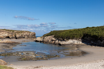 Secluded beach with rocky cliffs and calm water under a blue sky. Aerial view of coastal landscape with greenery and sandy shore