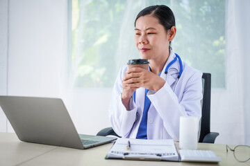 An Asian female doctor sits at her desk, conducting an online consultation. This faster, cheaper, and more convenient method helps prevent disease spread and offers easier access to healthcare.