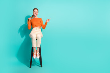 Full length photo of optimistic woman wear crop top sit on chair indicating at sale empty space isolated on turquoise color background
