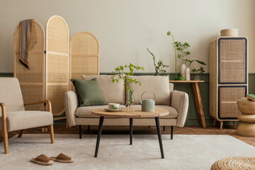 Creative composition of living room interior with beige sofa, wooden coffee table, rattan sideboard, partition wall, lamp, beige carpet, stylish armchair and personal accessories. Home decor. 