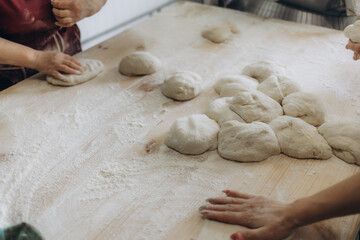 Unrecognizable young man kneading dough on wooden table. Males hands making bread on dark background. Selective focus.