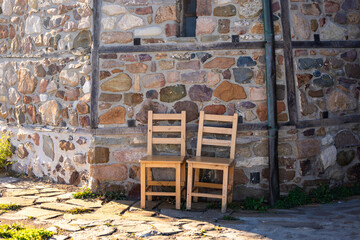 Two empty wooden chairs against an old stone wall on an island in the sea.