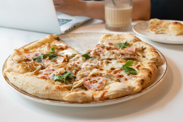Close-up photo of delicious pizza and man working on laptop on the background in the cafe