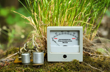 Electronic components and pointer indicator for measuring of environmental pollution level, placed in front of green grass bunch, growing on mossy surface, theme of environmental protection