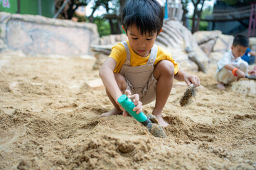 Asian kindergarten boy and girl enjoy playing in sandbox having fun on playground in sandpit.