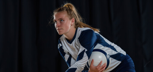 A young female volleyball player stands confidently with a volleyball in her hands. She is dressed in a team uniform and appears focused and ready for the game.