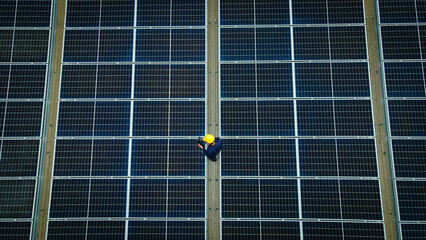 An engineer on roof meticulously inspects solar cell panels using a tablet and communicates...
