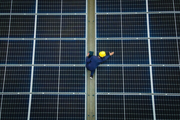 An engineer in a safety helmet and vest inspects solar panels on a rooftop, checking for efficiency...